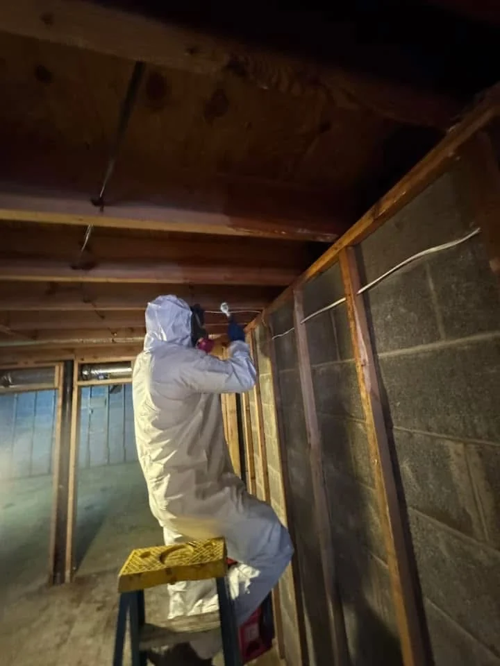 Technician in a protective suit and respirator working in an opened-up basement