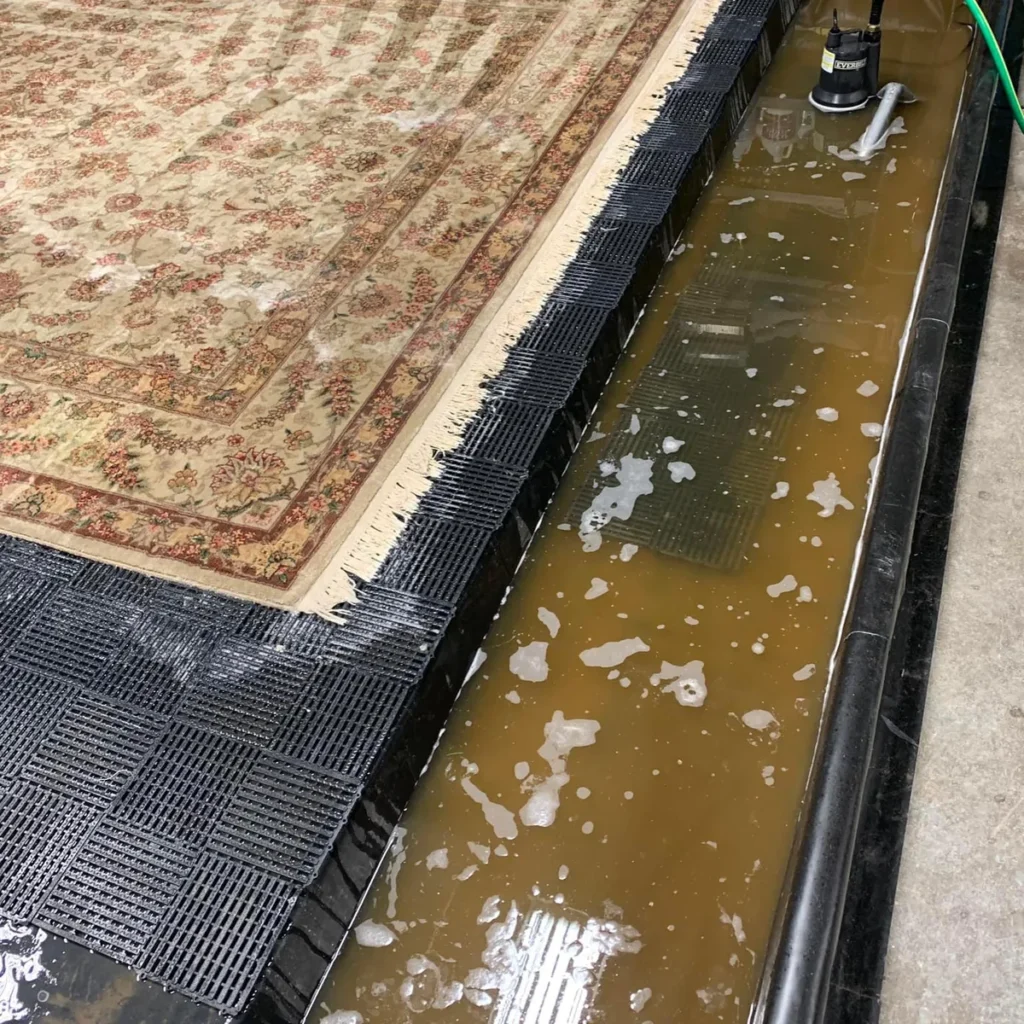 Area rug soaking in the wash pit, with dirty rinse water beside it